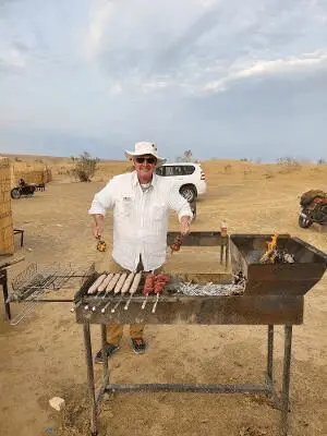 Man grilling sausages outdoors in desert.